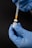 A close-up of a hand wearing blue gloves holding a vial labeled 'COMIRNATY' while a syringe is being inserted into it.