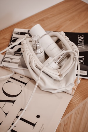 A neatly arranged collection of luxury skincare products placed inside an elegant white leather bag. The items are set against a backdrop of fashion magazines on a wooden surface, giving a sense of sophistication and style.