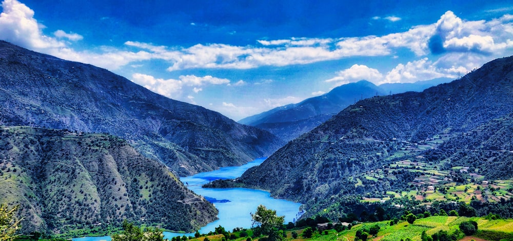 green and gray mountains beside body of water under blue sky and white clouds during daytime