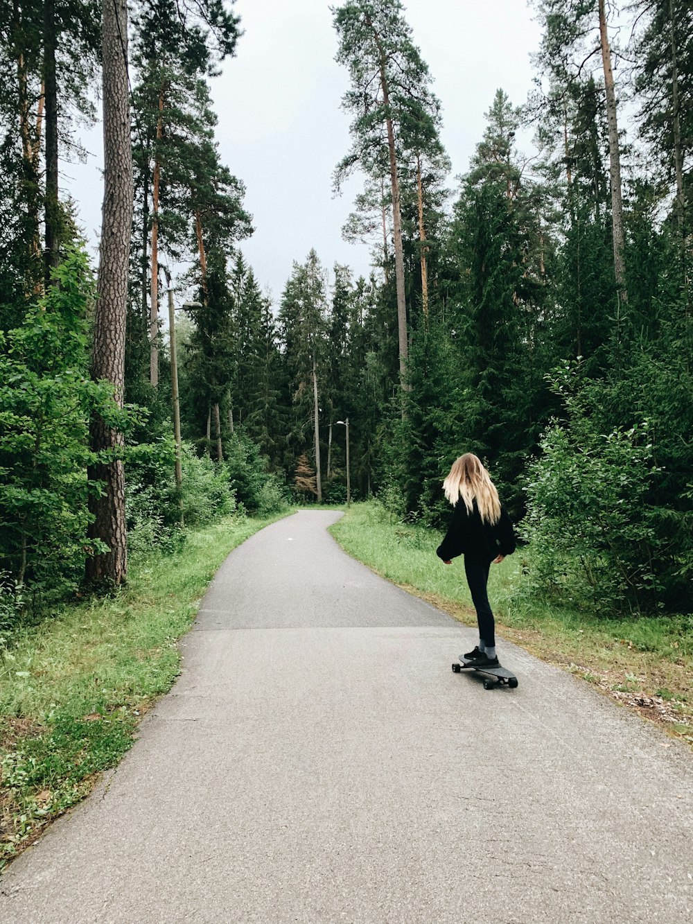 Mujer con chaqueta negra caminando por el camino de asfalto gris durante el día