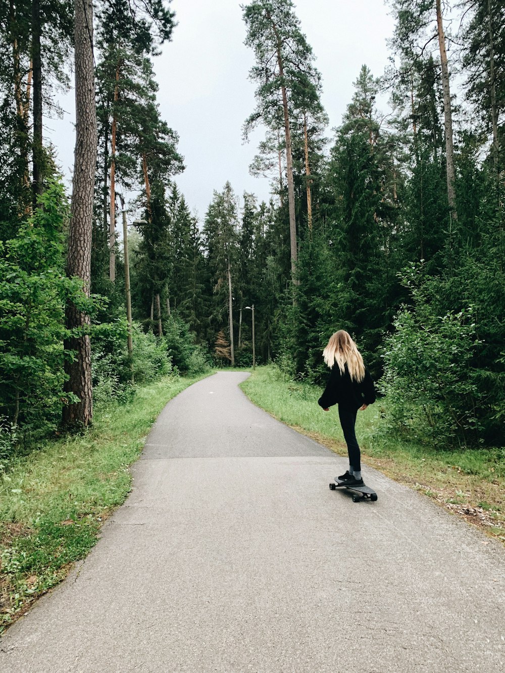 woman in black jacket walking on gray asphalt road during daytime