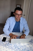 Photo of a man working on a laptop with eyeglasses beside him.