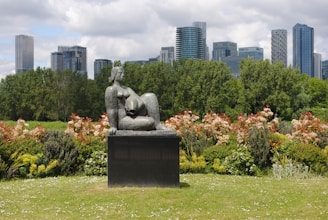 gray concrete statue on green grass field near green trees and high rise buildings during daytime