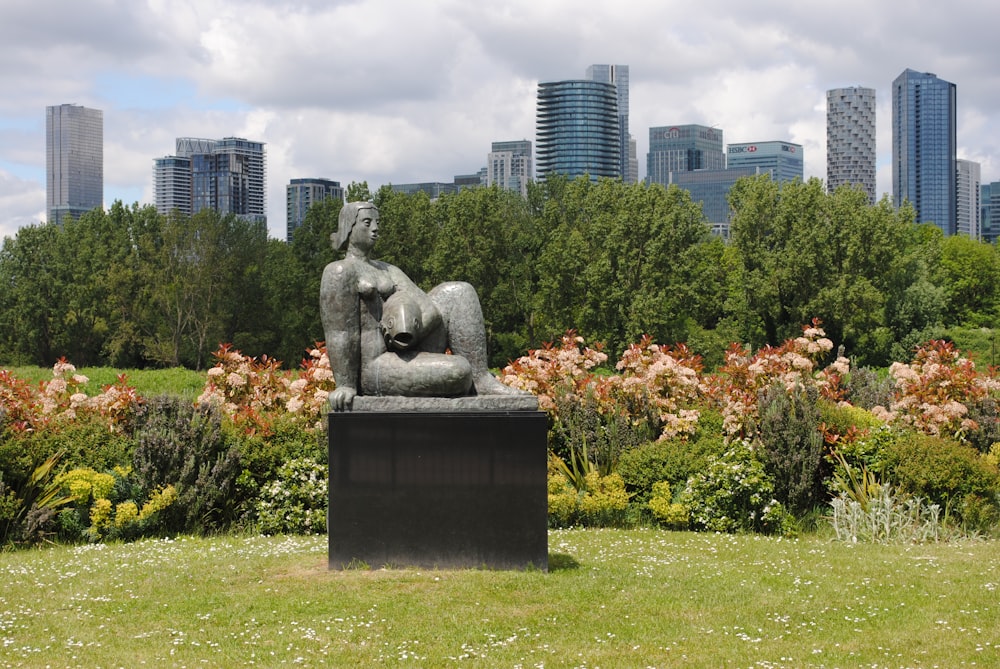 gray concrete statue on green grass field near green trees and high rise buildings during daytime