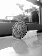 A close-up of a hand dropping a single rupee coin into a transparent piggy bank.