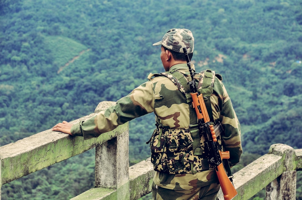 man in green and brown camouflage jacket holding black and brown rifle