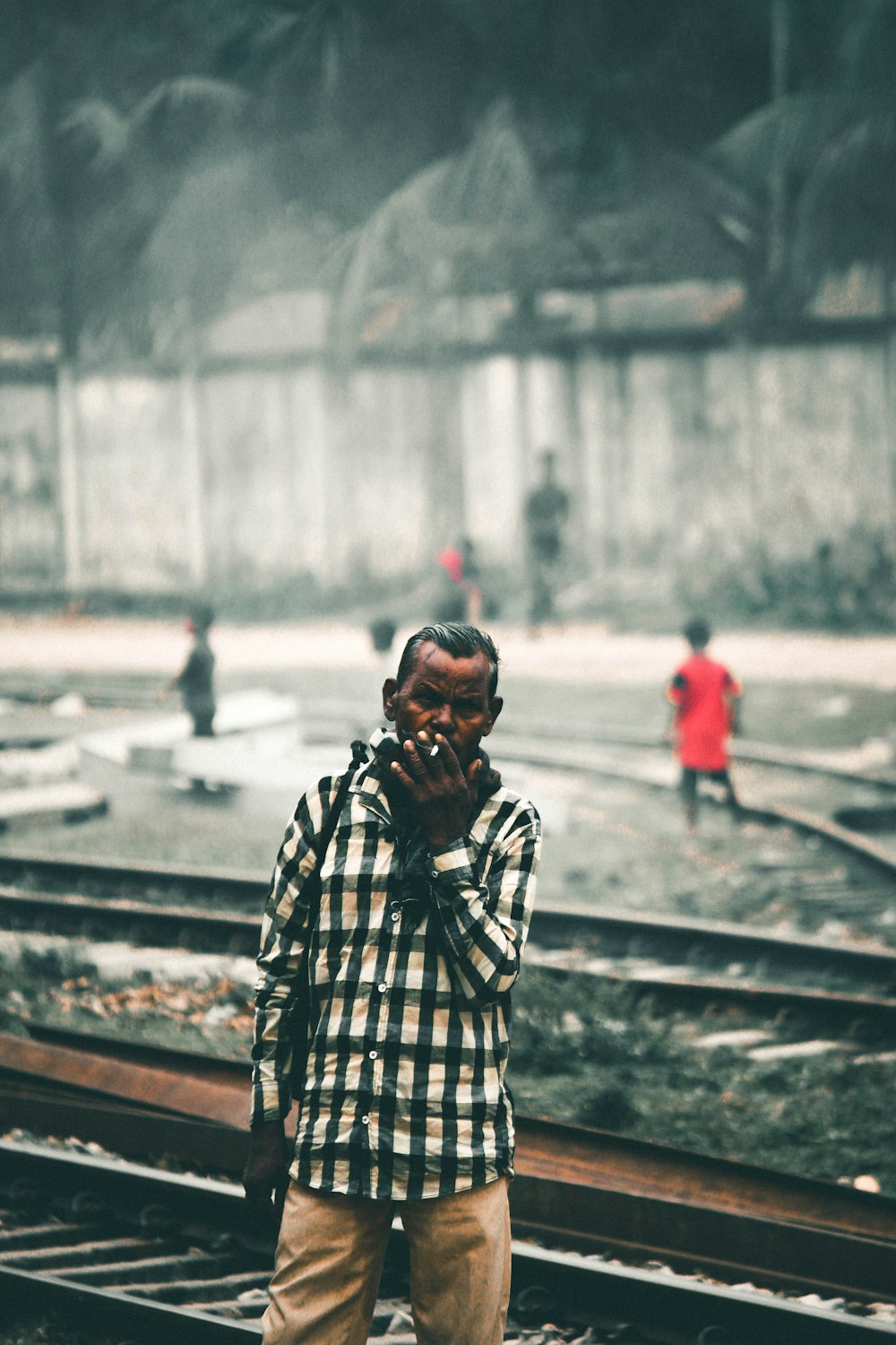 man in black and white plaid dress shirt standing on train rail during daytime