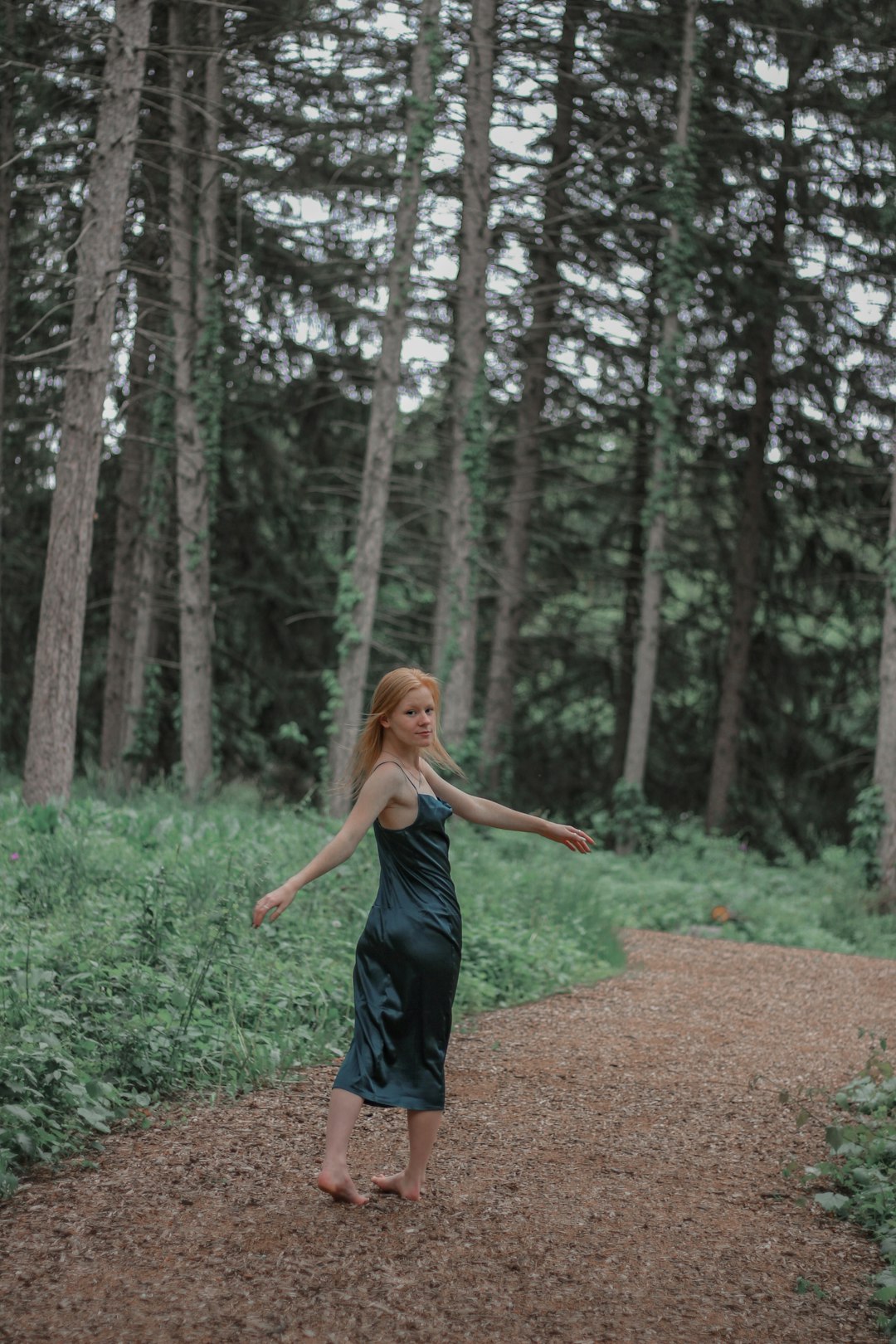 woman in black tank top and blue denim jeans standing on brown dirt road between green