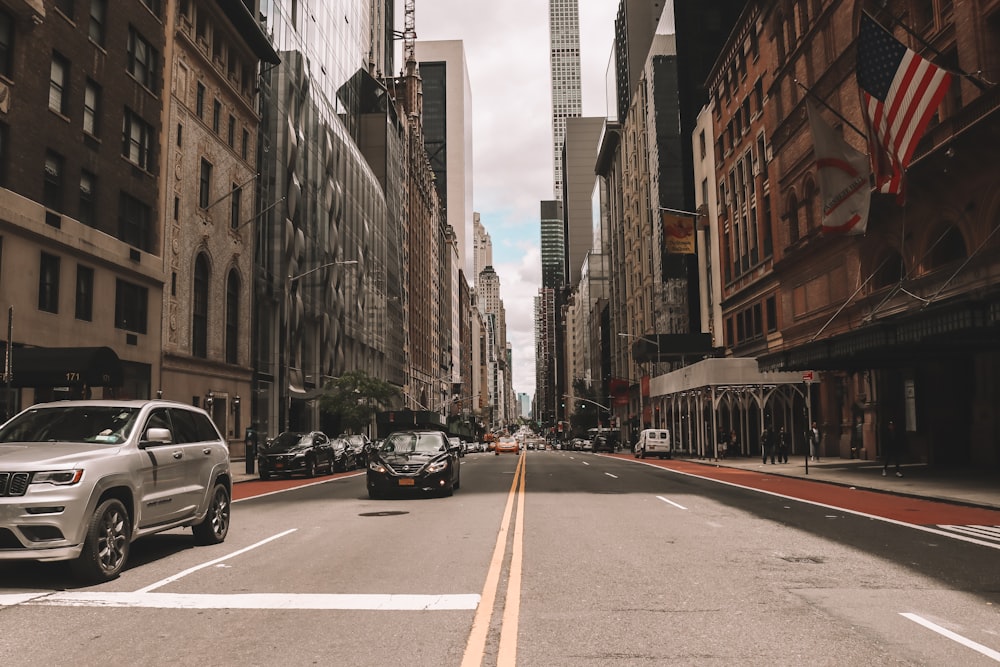 cars parked on side of the road in between high rise buildings during daytime