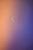 Soft focus image of a thin crescent moon symbol illuminated by warm, subtle light on a navy blue background.