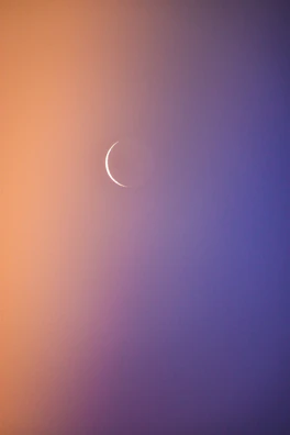 Soft focus image of a thin crescent moon symbol illuminated by warm, subtle light on a navy blue background.