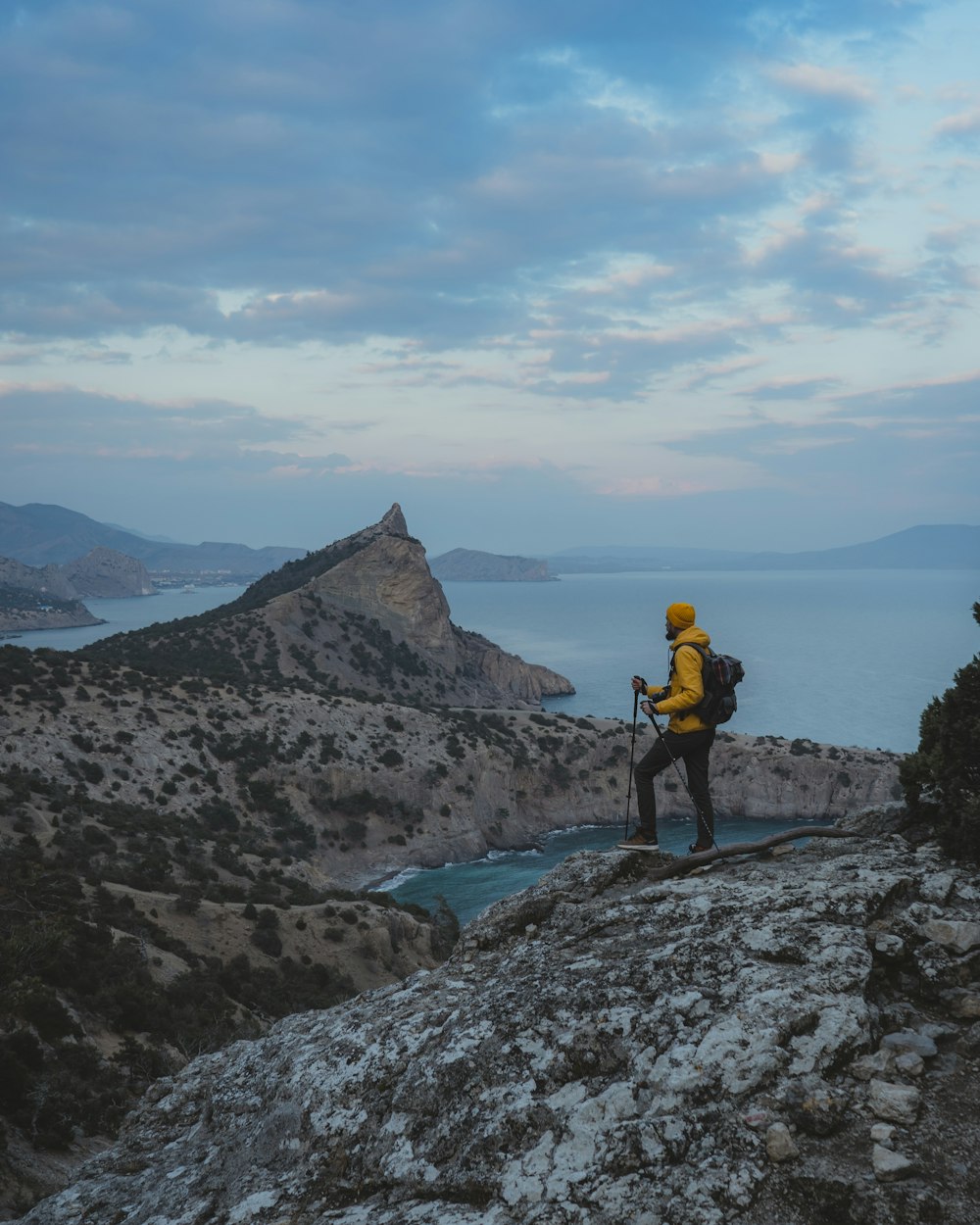 man in yellow jacket and black pants standing on rocky mountain during daytime