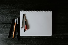 white spiral notebook with black pen