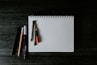 white spiral notebook with black pen