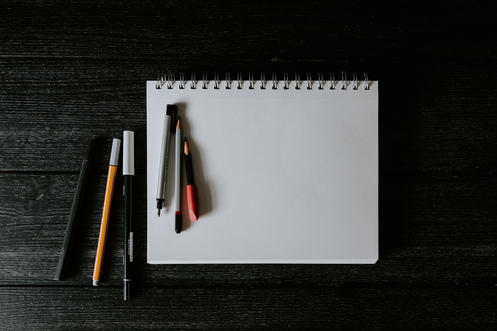 white spiral notebook with black pen