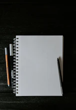 white spiral notebook beside orange pen