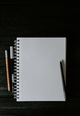 white spiral notebook beside orange pen