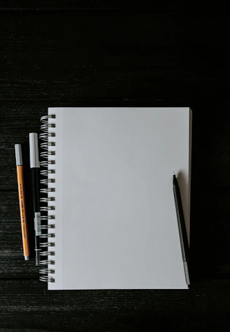 white spiral notebook beside orange pen