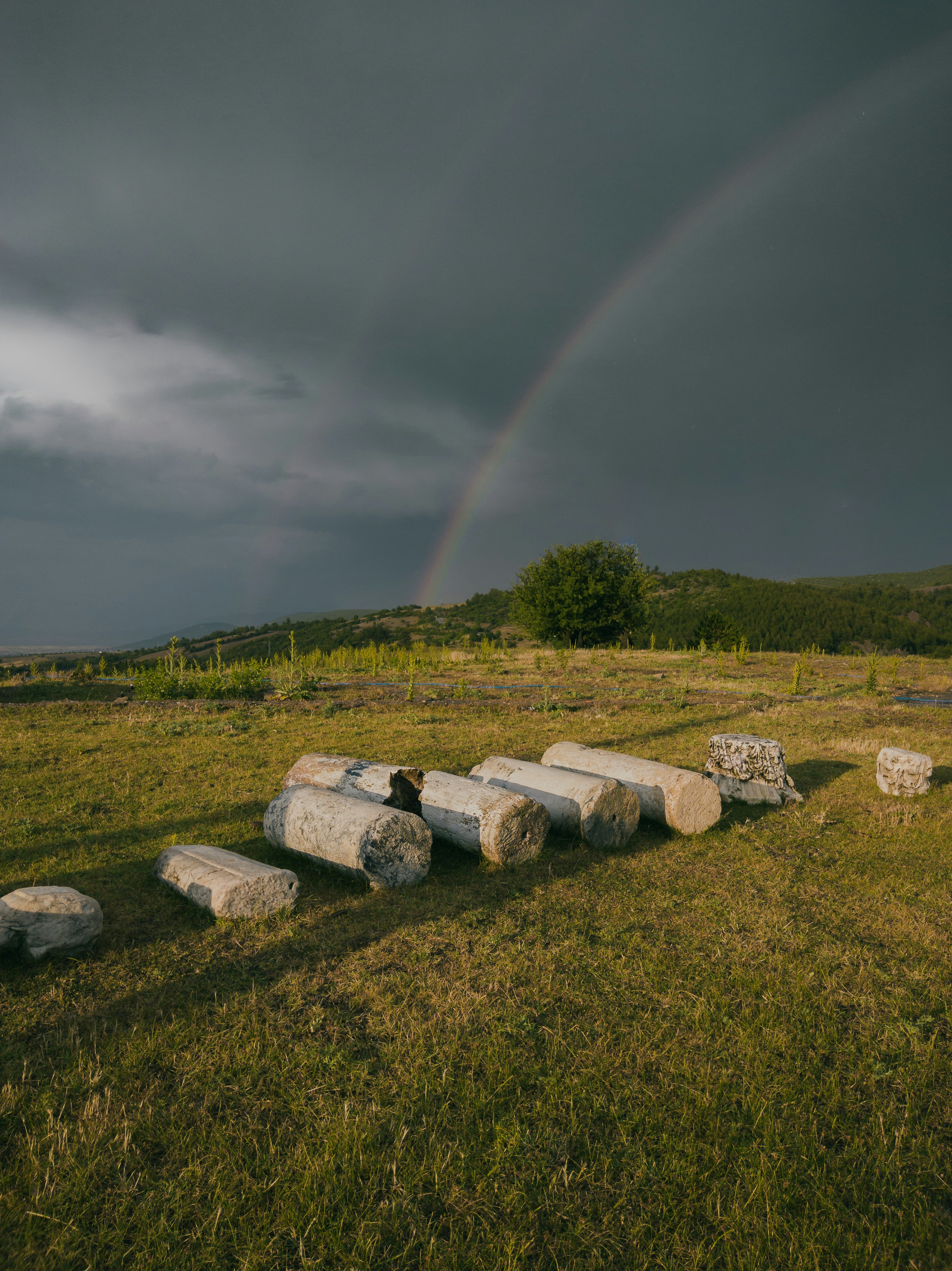 gray rocks on green grass field under rainbow