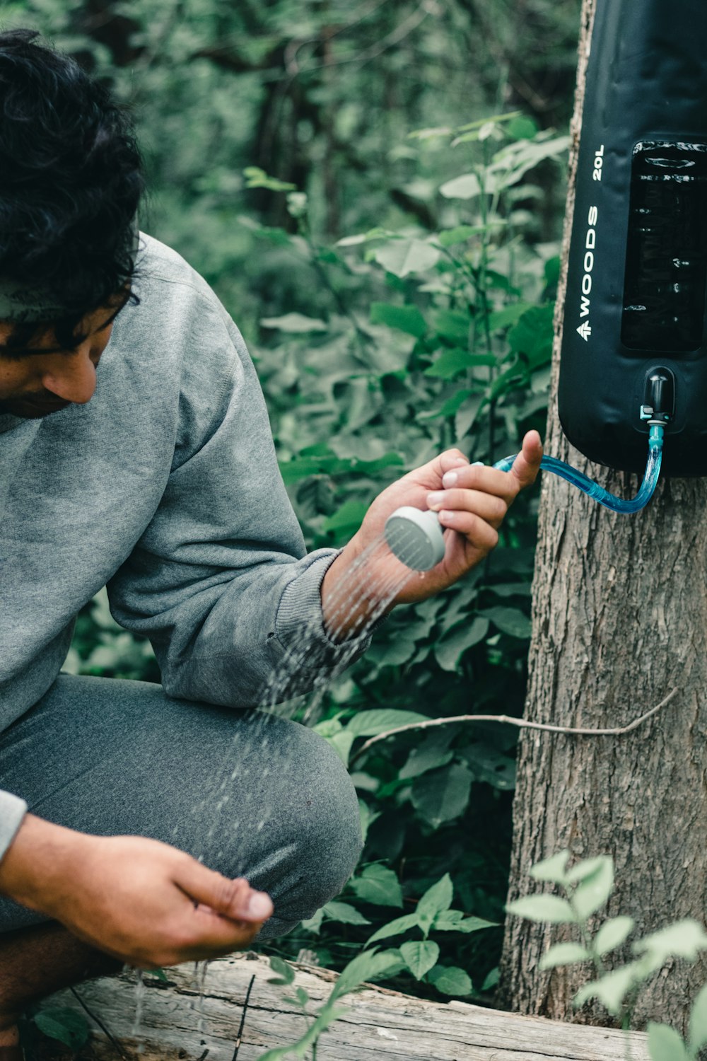 man in gray sweater and gray pants sitting on brown tree trunk