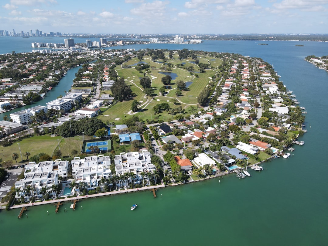 Aerial view of condos and luxury homes built around a golf course in the Normandy Shores Isles neighborhood of Miami Beach, waterfront homes looking out on a canal near Biscayne Bay. The city skyline can be seen in the distance.