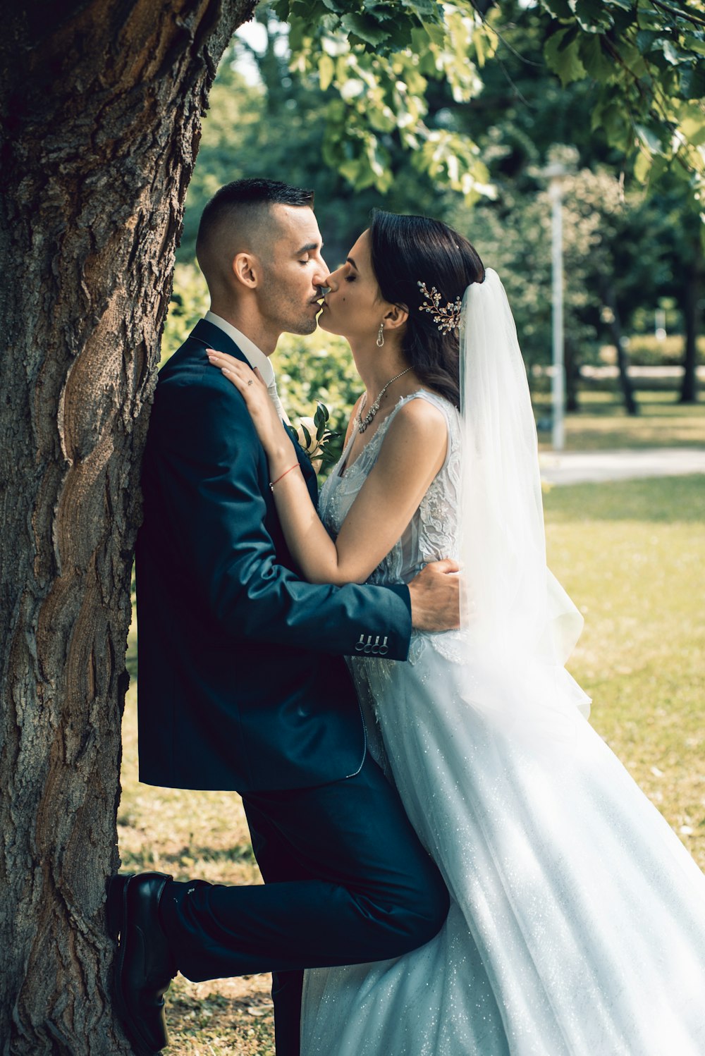 man in black suit kissing woman in white wedding dress near brown tree during daytime