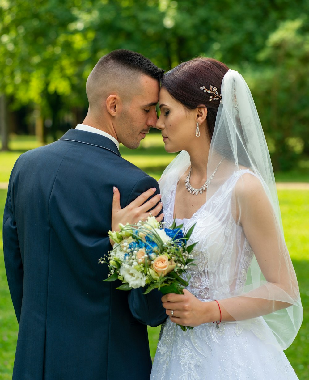 man in black suit kissing woman in white wedding dress on green grass field during daytime