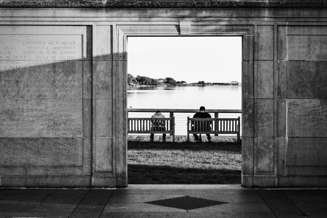 grayscale photo of people walking on sidewalk near body of water