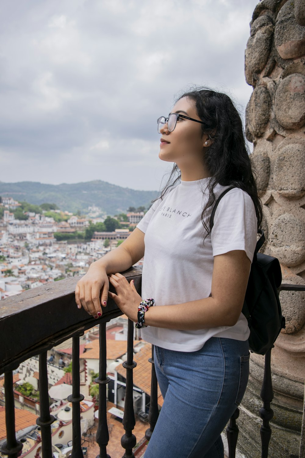 Mujer con camiseta blanca y jeans de mezclilla azul con gafas de sol negras de pie cerca de madera marrón