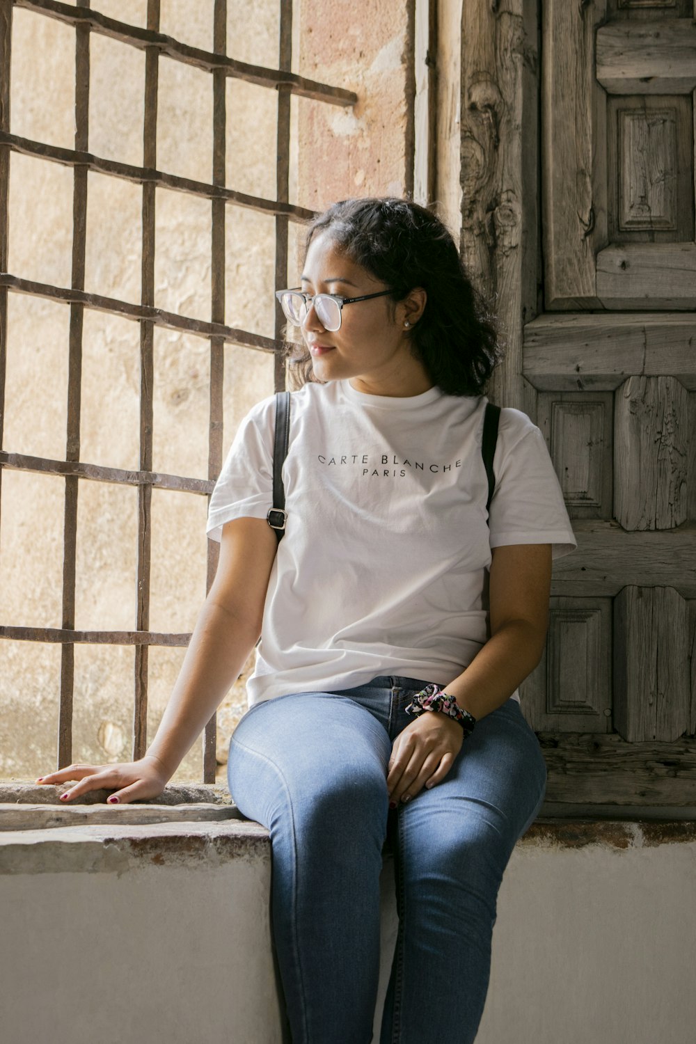 woman in white crew neck t-shirt and blue denim jeans sitting on brown wooden bench