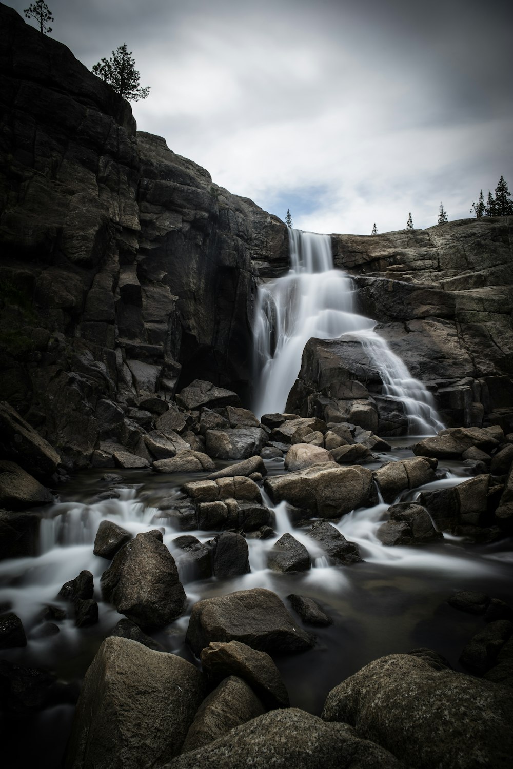 waterfalls on rocky mountain under cloudy sky during daytime