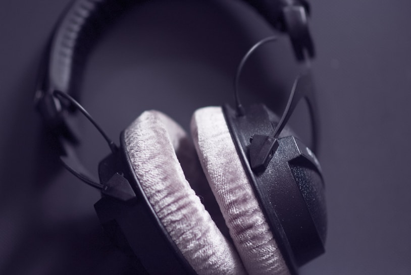 A pair of over-ear headphones with soft, plush ear cushions. The headphones are predominantly black with padded headband and visible wires on a dark background.