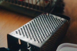 Close-up of a stainless steel grater and peeler resting beside fresh vegetables.