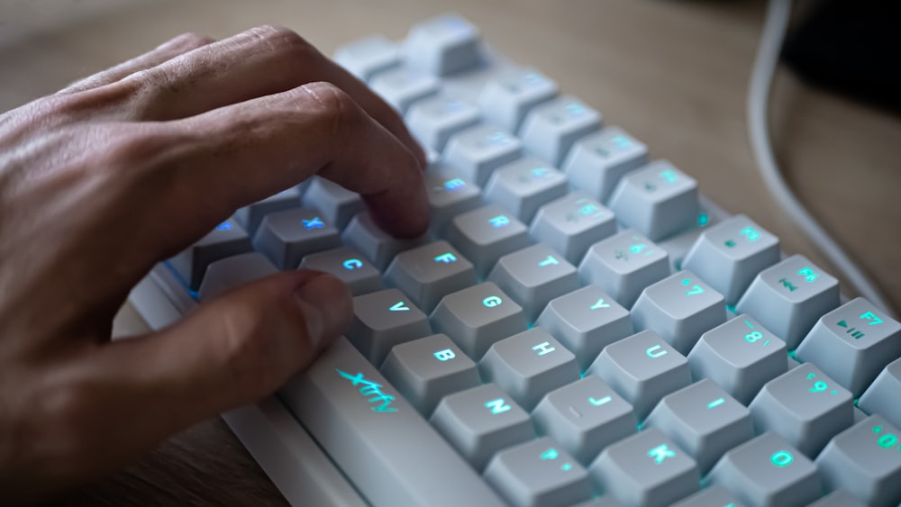 白と青のコンピューターキーボードに手を置いた人