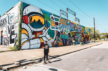 man in black jacket and black pants walking on sidewalk near graffiti wall during daytime
