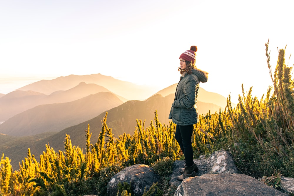 woman in green jacket standing on rock near yellow flower field during daytime