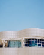 A modern architectural structure with smooth, curved lines and large, reflective windows. The building facade features a sleek, white grid design against a clear blue sky, creating a sense of openness and innovation.