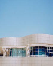 A modern architectural structure with smooth, curved lines and large, reflective windows. The building facade features a sleek, white grid design against a clear blue sky, creating a sense of openness and innovation.