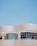 A modern architectural structure with smooth, curved lines and large, reflective windows. The building facade features a sleek, white grid design against a clear blue sky, creating a sense of openness and innovation.