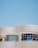 A modern architectural structure with smooth, curved lines and large, reflective windows. The building facade features a sleek, white grid design against a clear blue sky, creating a sense of openness and innovation.