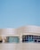 A modern architectural structure with smooth, curved lines and large, reflective windows. The building facade features a sleek, white grid design against a clear blue sky, creating a sense of openness and innovation.
