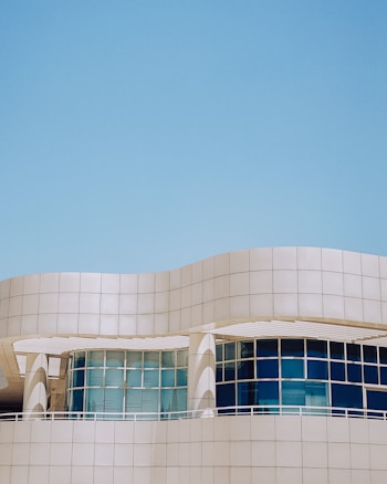 A modern architectural structure with smooth, curved lines and large, reflective windows. The building facade features a sleek, white grid design against a clear blue sky, creating a sense of openness and innovation.