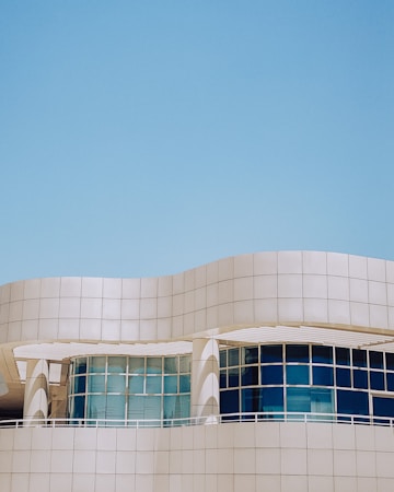 A modern architectural structure with smooth, curved lines and large, reflective windows. The building facade features a sleek, white grid design against a clear blue sky, creating a sense of openness and innovation.