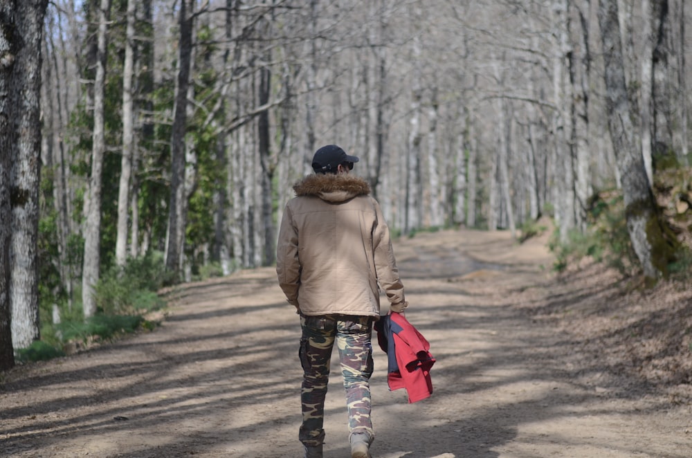 person in brown jacket walking on pathway in the woods during daytime