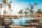 A luxurious outdoor swimming pool area surrounded by tall palm trees and various lounge chairs. Bright orange umbrellas add a pop of color, creating a vibrant and inviting atmosphere. The sky is clear and blue, enhancing the tropical feel.