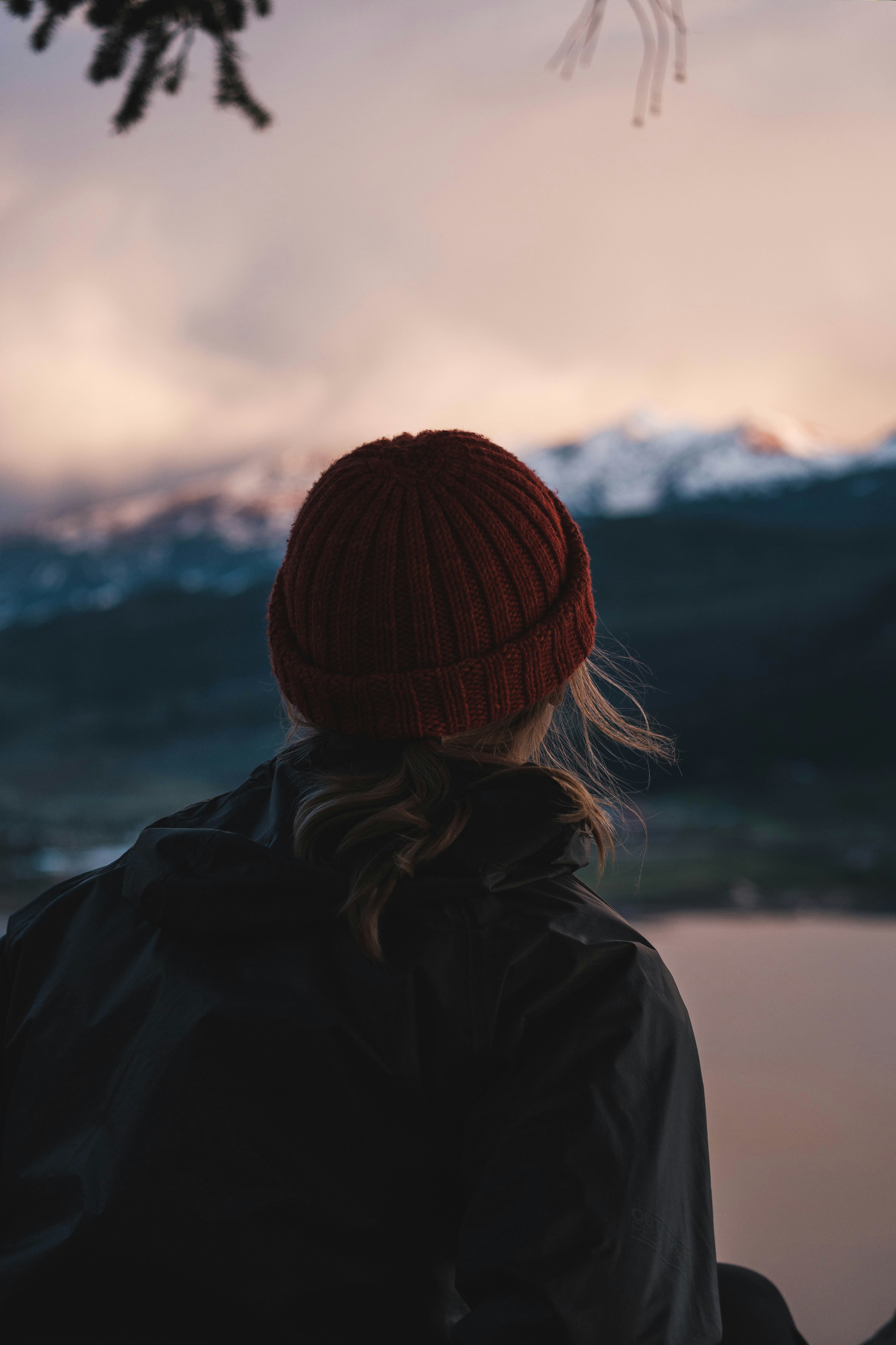 woman in black jacket and orange knit cap looking at the mountains during daytime
