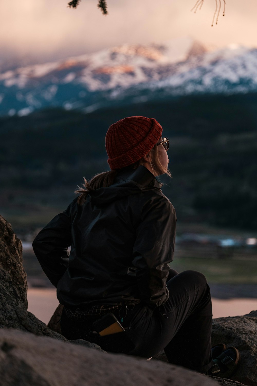 person in black jacket and red knit cap sitting on brown rock during daytime