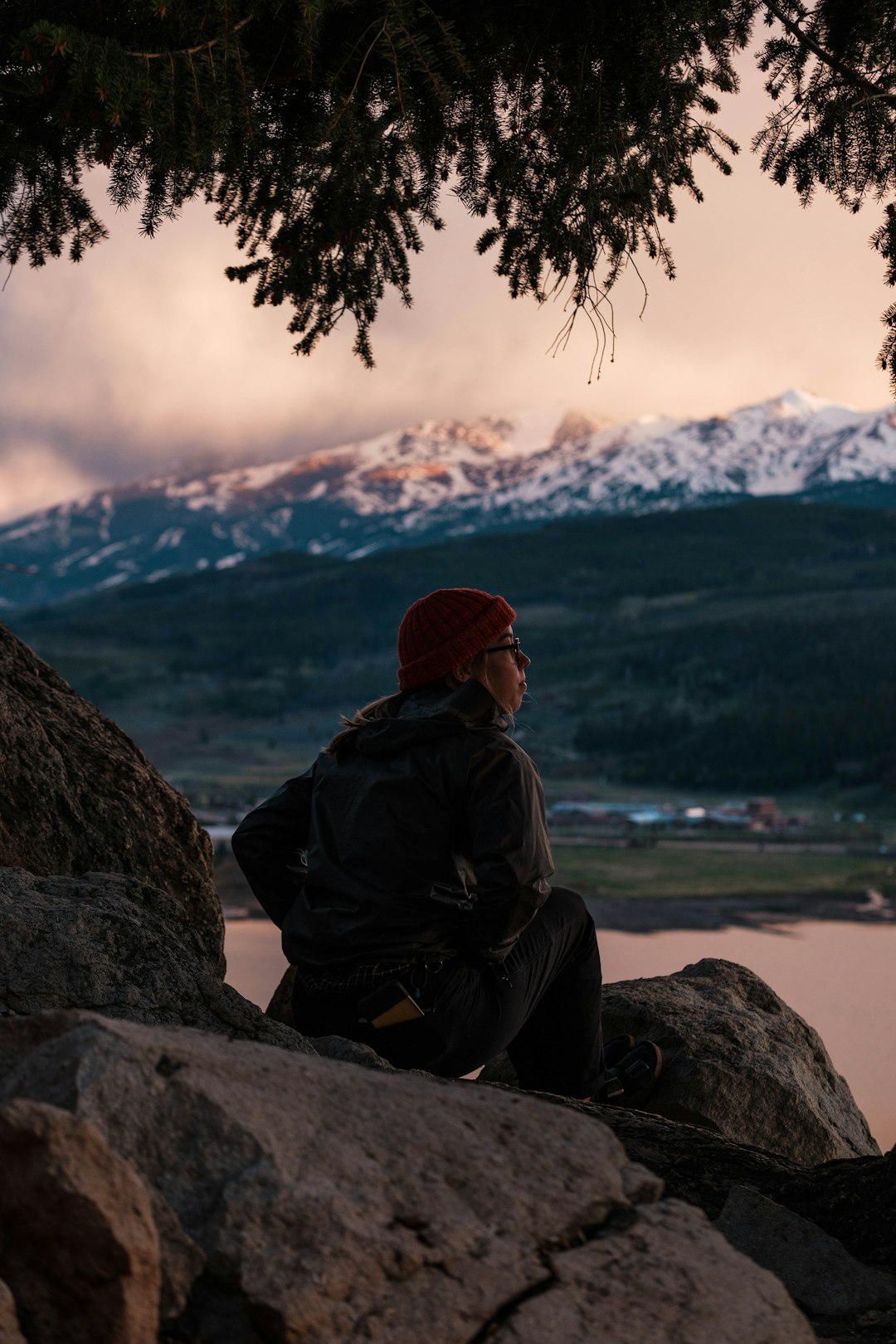 man in black jacket sitting on rock near body of water during daytime