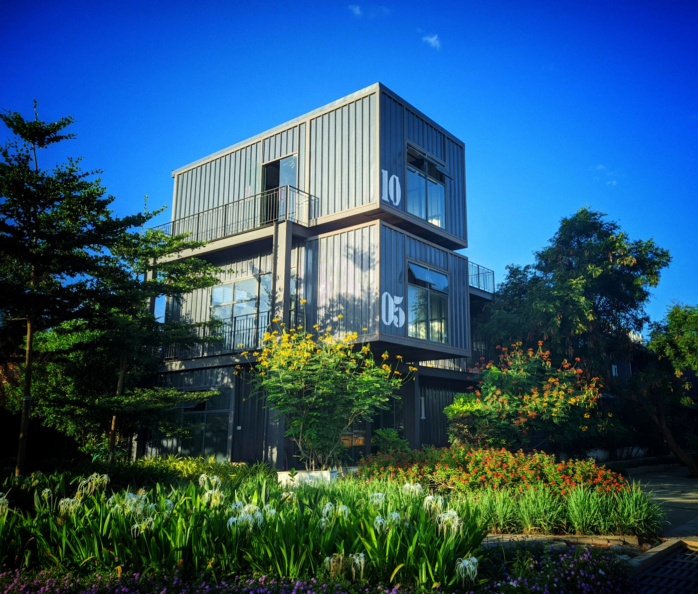 Multi-story building constructed from stacked shipping containers with plants around it