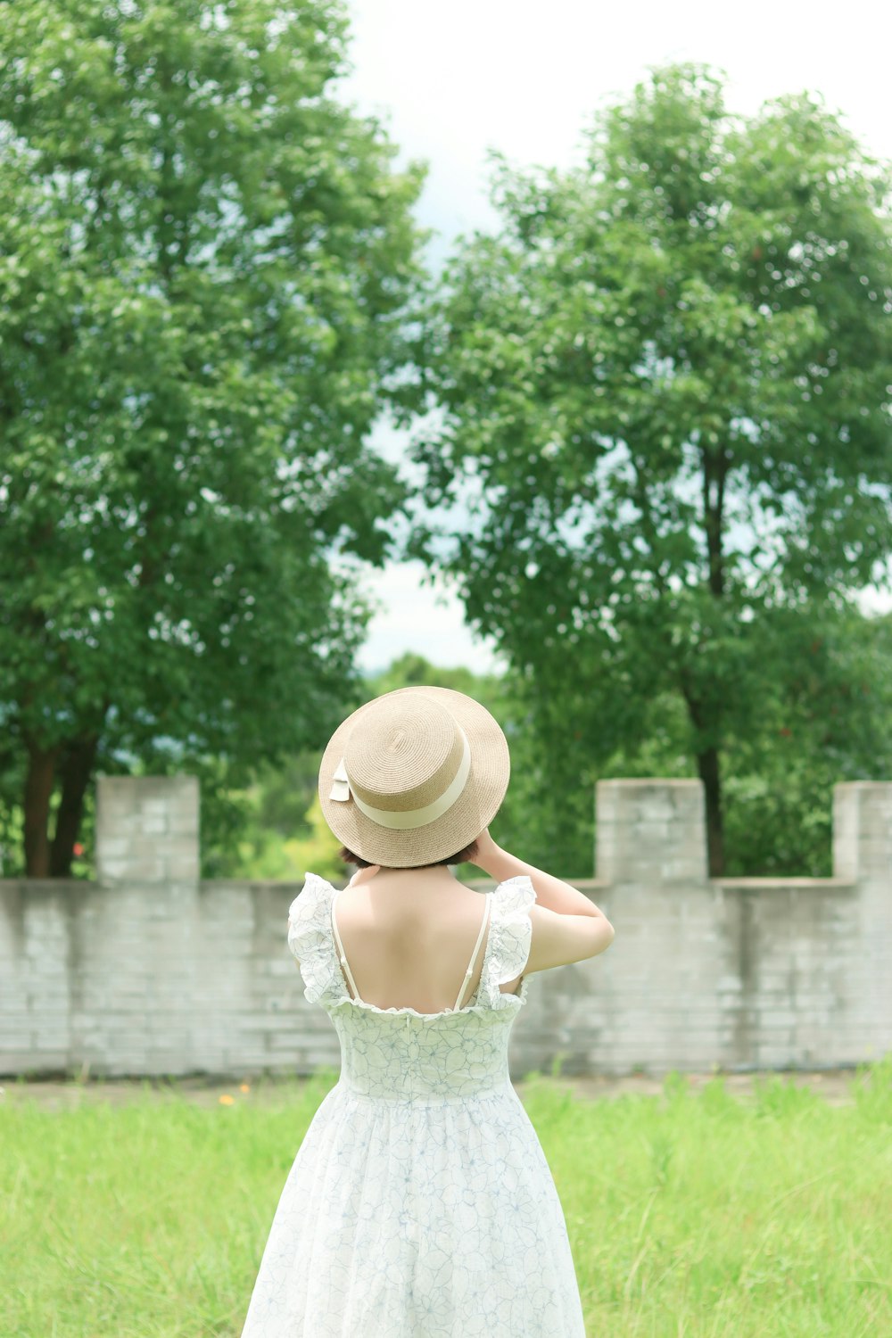 woman in white floral lace dress wearing brown sun hat standing on green grass field during